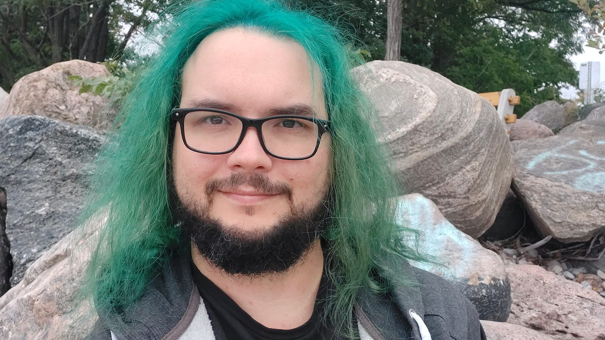 A man with green hair stands outside at a boulder breakwater, photo 1